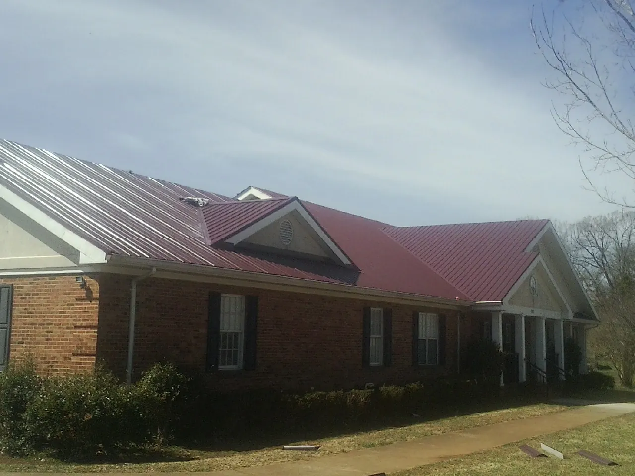 Red metal roof with gabled entries on a long brick building, from a Hail Damage Roof Repair job in Ouray