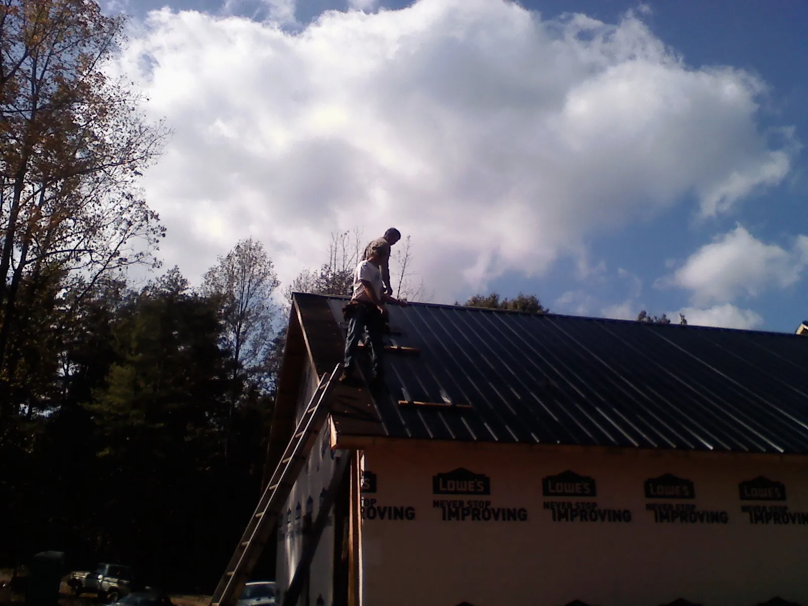 Roofer fastening dark metal panels high against a cloudy sky, from a Roof Inspection job in Ouray